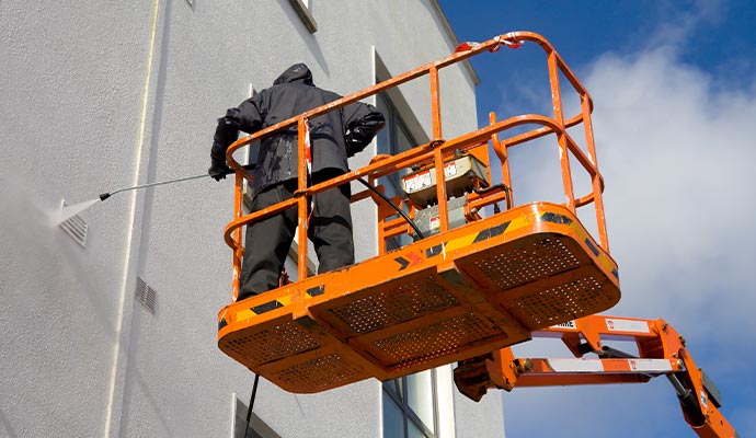 person cleaning building exterior with pressure  on cherry picker