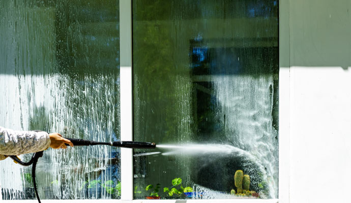 A person using a pressure washer to clean a dirty window