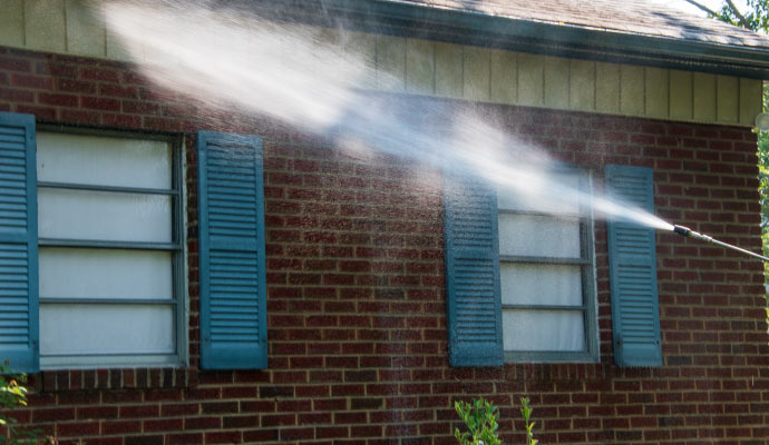 A person is pressure washing a brick house