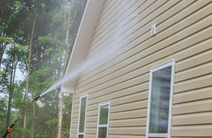 A person is pressure washing the siding of a house. 