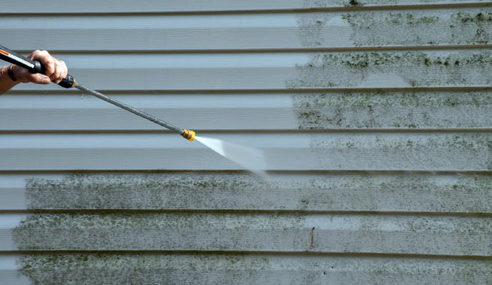 A person pressure washing the side of a house