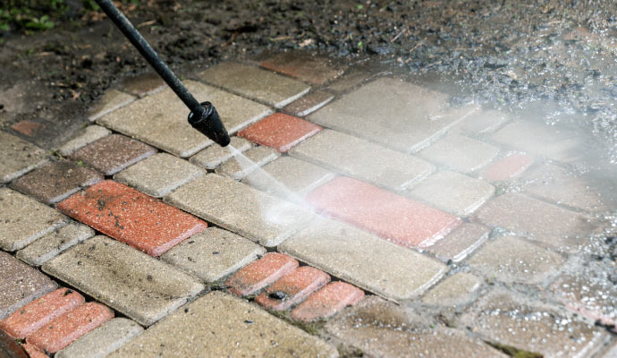 A pressure washer is cleaning interlocking pavers