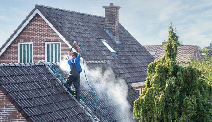 A professional cleaning a roof with pressure water hose